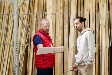 Shop assistant of hardware store helping young man to choose wooden board