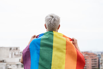 Senior man wearing lgbt rainbow flag with city in background - Focus on face