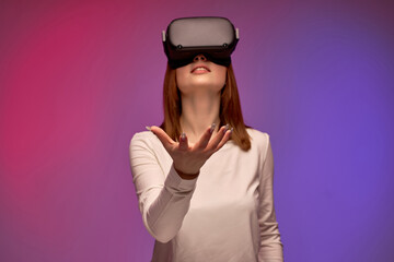 excited young female in virtual reality helmet, looking into VR glasses screen. Young caucasian woman is surprised by reality VR helmet, holds out hand forward. portrait. modern technologies concept