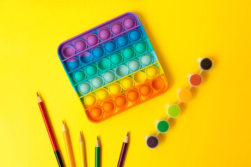 Naklejka premium Top view of the new sensory toy - rainbow pop it with children stuff on the sides - multicolor pencils and paints.Antistress toy for child and adult.
