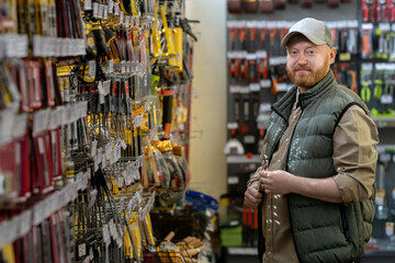 Bearded male customer with handtool standing by display with household goods