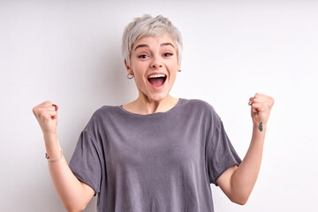 Excited young woman with short hair celebrating the win, cheering with raised arms, screaming, happily looking at camera, isolated on white background. win, celebration, holiday, luck concept