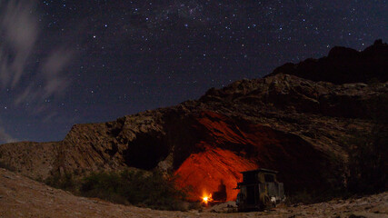 Black shadow of person camping in a cave.   It is night time and stars are visible in the sky. The...