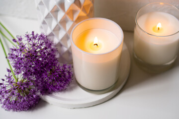 Fototapeta na wymiar Burning candle and violet allium flowers on white tray