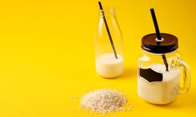 Vegan drink for breakfast. Rice alternative milk in glass bottle and mug on yellow background. Gluten and lactose free healthy food concept. Copy space.