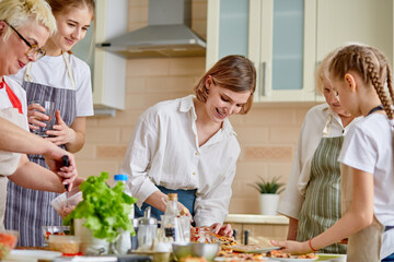 Side view portrait of attractive ladies grandmoms and children cooking. making dough and ingredients for pizza and other meal, wearing apron. at home in kitchen