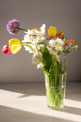 bouquet of colorful bright garden flowers in vase in sun light on white table