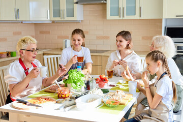 Side view portrait of young generation with grandmothers talking over cup of tea at home, in apron, after cooking. portrait of beautiful females having conversation, discussing and drinking tasty tea