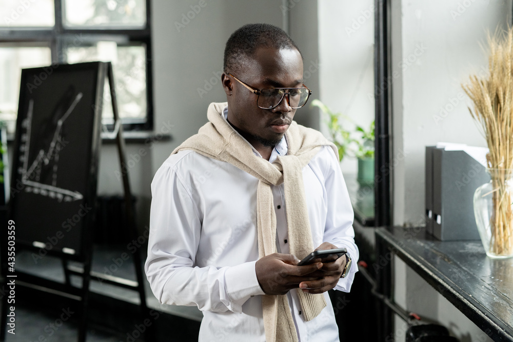 Wall mural young businessman of african ethnicity scrolling in smartphone in office