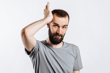 Fototapeta premium Portrait of handsome young man frowning while holding hands near head on white background with space for advertising mock up