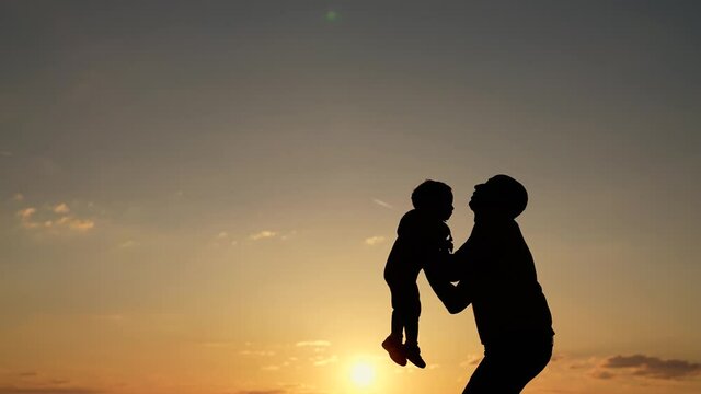 Silhouette of happy family. Father and son in park. Father tosses son up. Happy family concept. Father plays with son in park. Family silhouette. Father tosses his son up. Silhouette of happy family