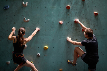 Two active sporty man and woman compete on speed bauldering championship indoors, climbing on...