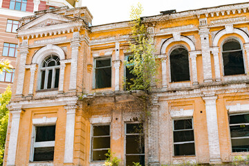 Fototapeta na wymiar Yellow old classical facade of historical house with trees growing on the balcony. Damage. Destroy. Architectural. Heritage. History. Home. Facade. External