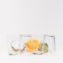 Glass cups on a white background and behind them is coconut, orange and kiwi. Copy space.