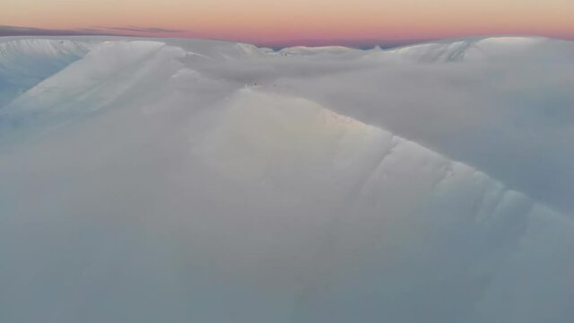 Snow-covered ridge of the mountain range in the clouds at sunset. Gentle evening light in the mountains in winter. Drone shooting.