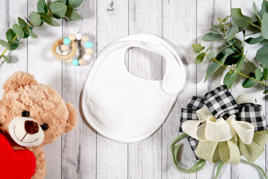 Baby wear bib flatlay. On-trend farmhouse theme craft product mockup with farmhouse style decor, on a white wood background. Negative copy space for your design here.