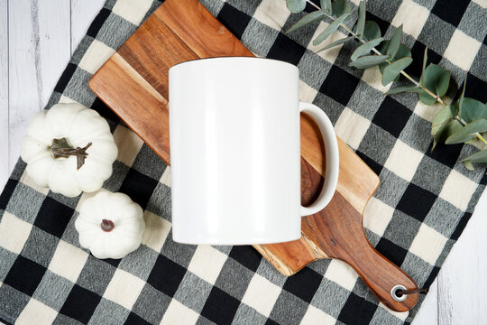Kitchen supersize coffee mug mockup. On-trend farmhouse aesthetic flatlay svg craft product mock up with black plaid table cloth and white pumpkins on a white wood background. Negative copy space.