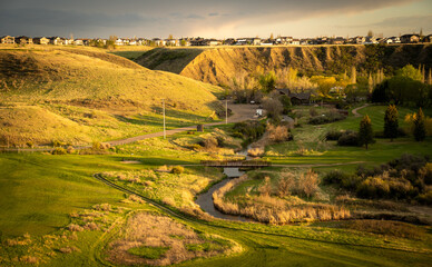 A golf course in Seven Persons Coulee in Medicine Hat Alberta Canada with a spring creek and pedestrian bridge at dusk.