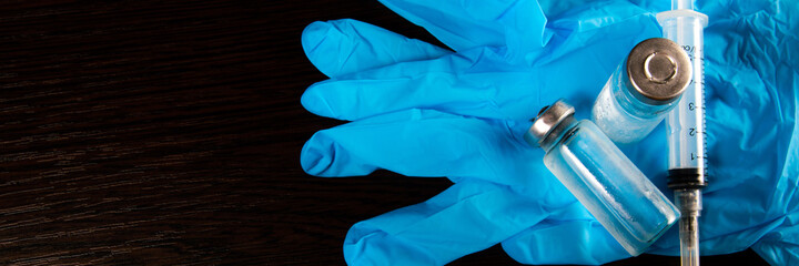 2 doses of Sars-Kov-2 coronavirus vaccine in transparent glass ampoules, covered with frost and a disposable syringe, on a dark background, short focus, toning