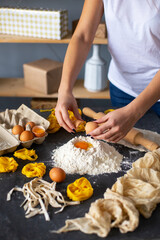 Obraz na płótnie Canvas Closeup of process of making homemade pasta. Woman preparing dough for pasta. A woman breaks an egg into a mound of flour 