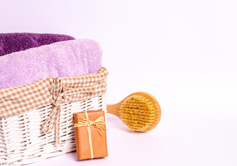 Colored terry towels in a basket, a wooden massage brush, soap on a white background.