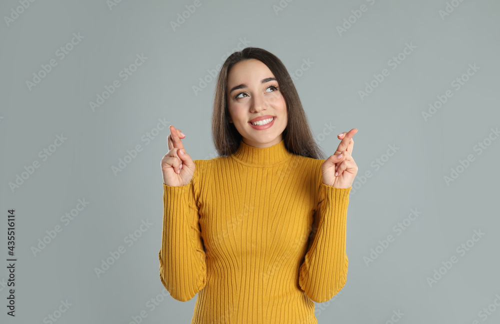 Wall mural Excited young woman holding fingers crossed on grey background. Superstition for good luck