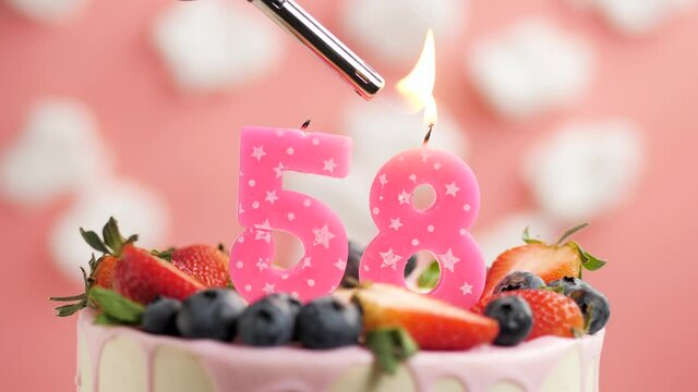Birthday cake candle number 58. Candle and cake on pink background and fire by lighter. Close-up and slow motion