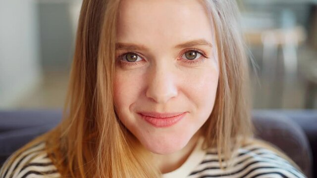 Closeup portrait of beautiful young woman with green eyes, natural blonde hair and in striped sweatshirt looking at camera, smiling and laughing at home