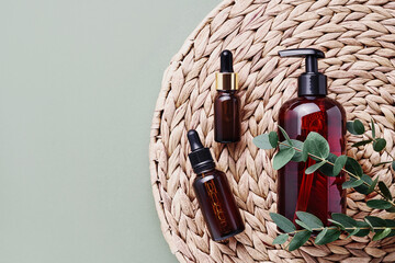 Dropper bottles of essential oil or serum, eucalyptus branches and dark dispenser bottle of shower gel. SPA concept.