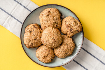 Close up top view on crunchy oatmeal chip cookies fresh baked biscuits with chocolate and cocoa in a plate on the yellow modern abstract background - homemade food concept
