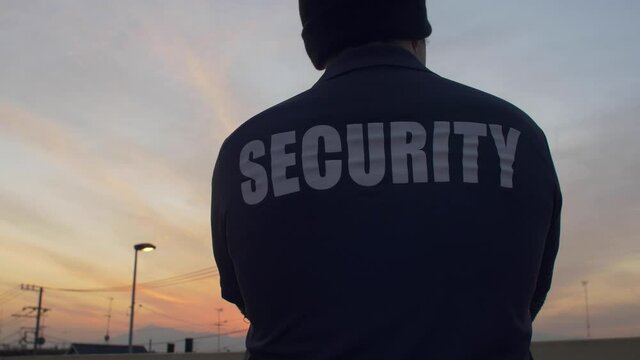 A rearview of security personnel standing and observing on a footbridge at sunset in 4K