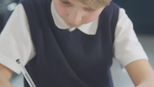 Boy at home wearing school uniform doing maths homework on kitchen counter - shot in slow motion