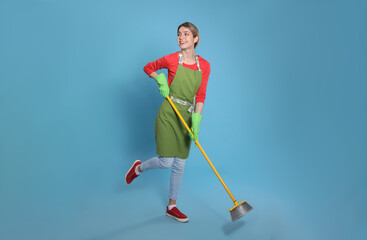 Obraz premium Young housewife with broom on light blue background