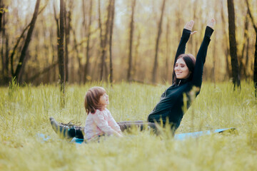 Cheerful Mother Exercising with her Child Outdoors on Yoga Mat