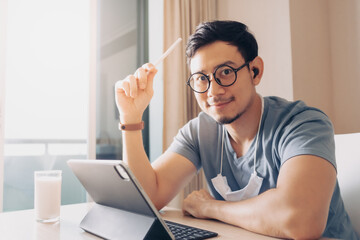 Happy Asian man is working on his tablet in concept of work from home.