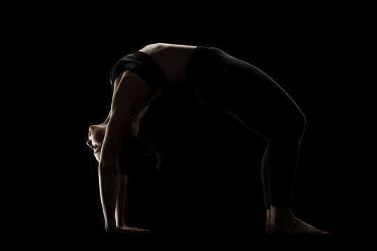 cute caucasian girl exercising yoga poses against dark backgroung. side lit silhouette. © Nikola Spasenoski