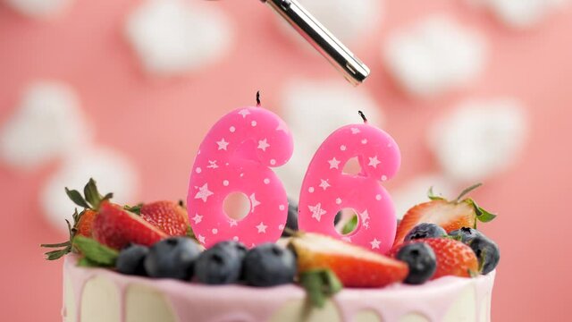 Birthday cake candle number 66. Candle and cake on pink background and fire by lighter. Close-up and slow motion