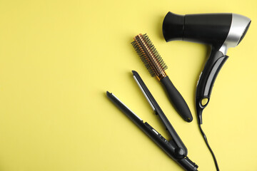 Hair dryer, straightener and brush on yellow background, flat lay. Space for text
