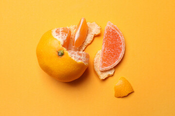 Fresh tangerine with one jelly candy as its segment on orange background, flat lay. April Fools' Day