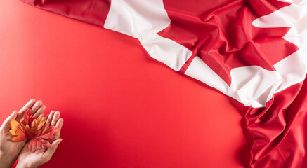 A beautiful Canada national flag cloth fabric with hand holding maple leaf against red background. A sign or symbol of Canada day concept.