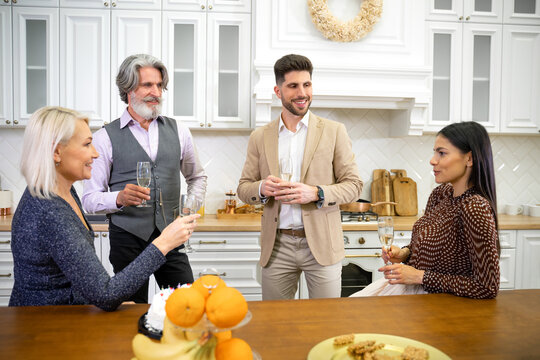Loving young daughter making toast while celebrating her father's birthday holding glass of champagne while sitting in kitchen at home together with mother and husband. Family celebration concept