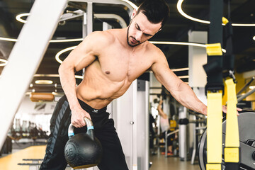 Fototapeta na wymiar Handsome young sports man bodybuilder with naked torso doing exercises with kettlebell in the gym