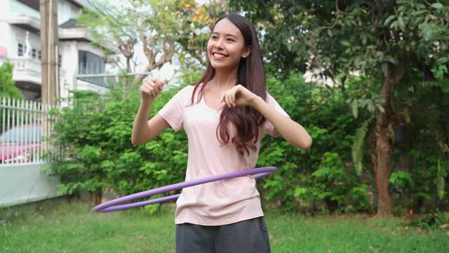 Asian girl doing exercise by using hula hoop in front yard at home.
