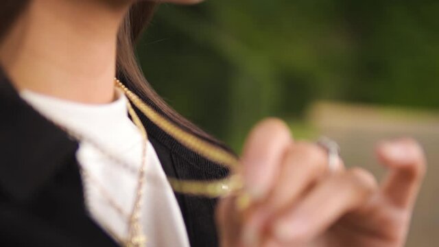 close up shot of a young caucasian woman touching her golden necklace jewellery wearing silver rings stiting on a bench feeling nostalgic relaxing by herself isolated blurry backround slow motion