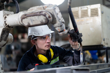 Male engineer holding robot controller for maintenance or repair automatic robotic machine in...