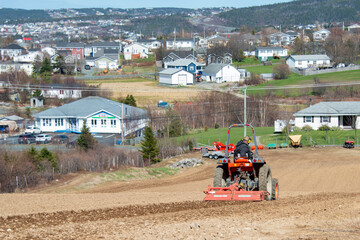A small red farm tractor with a male farmer riding on the equipment. The field has been cultivated...