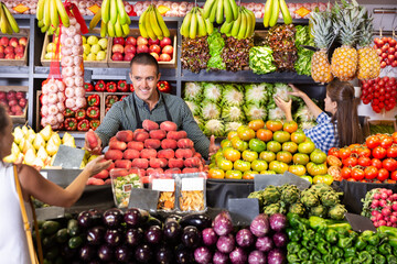 Obraz premium Portrait of young male in apron offering fresh peaches to woman customer at the market