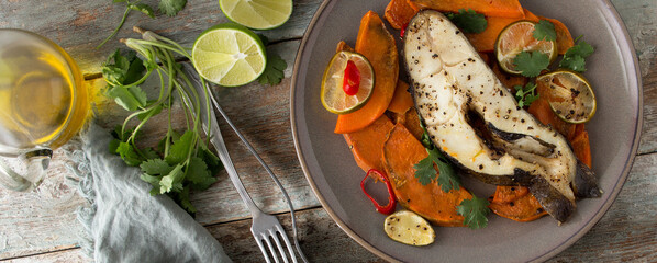 flat lay of plate with halibut steak baked with sweet potato, lime and chili on wooden table
