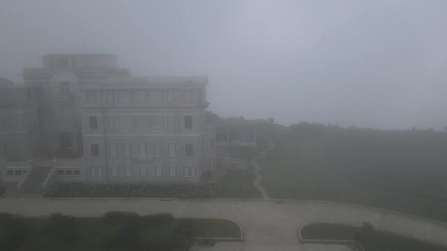 Drone footage above the iconic Bokor Hotel. Camera is sliding from right to left and the architecture is 
surronded by clouds and fog and gives a ghost vision of the building.