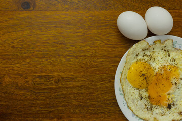Two raw eggs kept next to a plate serving single fried eggs with empty copy space 